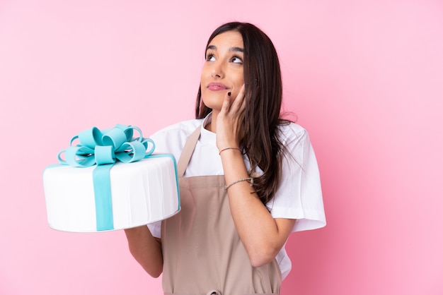 Jonge vrouw met een grote cake over geïsoleerde muur