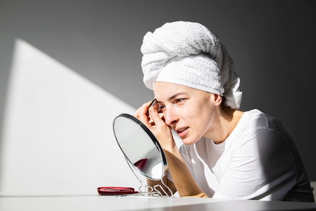 Jonge vrouw met een handdoek op haar hoofd plukt haar wenkbrauwen