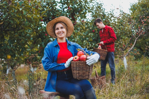 Jonge vrouw met een hoed in een appelboomgaard Vrouwen met hoeden verzamelen rode appels in een mand op de achtergrond van de natuur Het oogsten van appels in de tuin Het herfstseizoen in de boomgaard