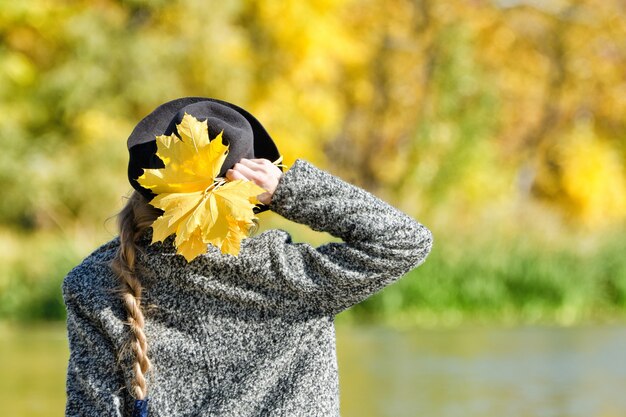 Jonge vrouw met een hoed met een bos bladeren staat op de oever van de rivier