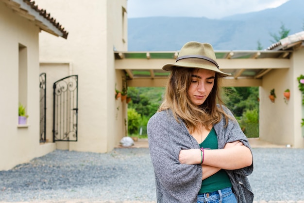 Jonge vrouw met een hoed met een melancholieke uitdrukking met koloniale architectuur op de achtergrond