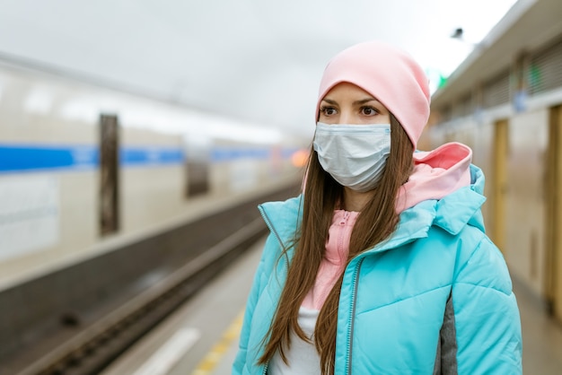 Jonge vrouw met een kaukasisch uiterlijk in warme kleren in de metro met een beschermend masker tegen de v...