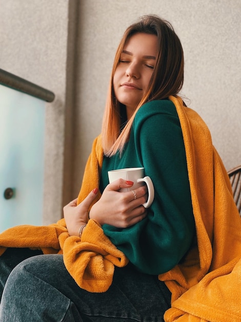 Jonge vrouw met een koffiekop met gesloten ogen die thuis zit