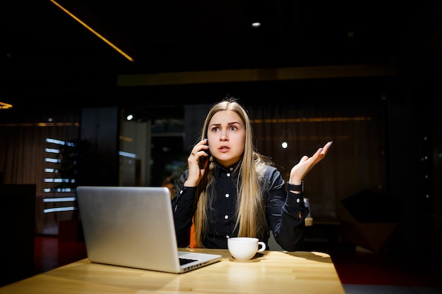 Jonge vrouw met een kopje koffie en met behulp van laptopcomputer praten aan de telefoon. Zakenvrouw die vanuit huis werkt. Thuiswerken