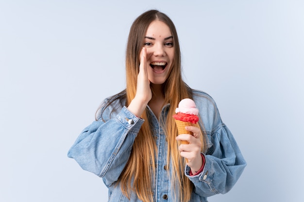 Jonge vrouw met een kornetijs dat op blauwe muur wordt geïsoleerd die met wijd open mond schreeuwt