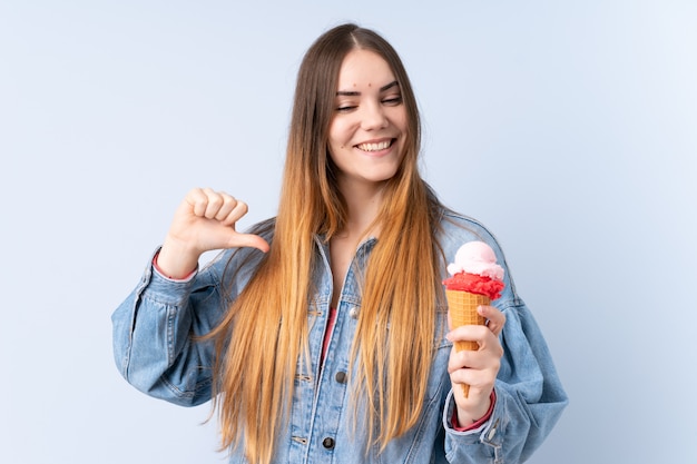 Jonge vrouw met een kornetijs dat op blauwe trots en zelfverzekerde muur wordt geïsoleerd