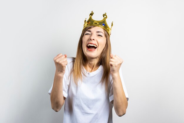 Jonge vrouw met een kroon op haar hoofd verheugt zich emotioneel en viert op een lichte achtergrond