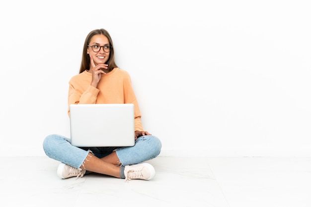 Jonge vrouw met een laptop die op de grond zit en een idee denkt terwijl ze omhoog kijkt