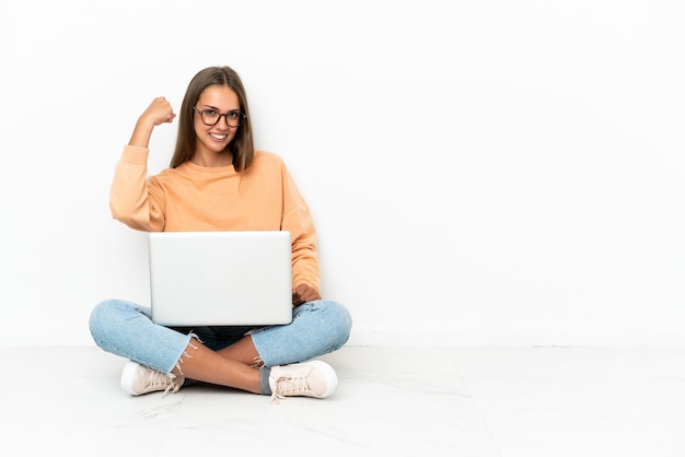 Jonge vrouw met een laptop die op de grond zit en een sterk gebaar doet