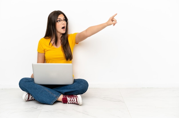 Jonge vrouw met een laptop die op de grond zit en wegwijst