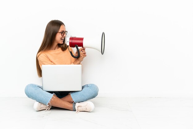 Jonge vrouw met een laptop die op de grond zit te schreeuwen door een megafoon