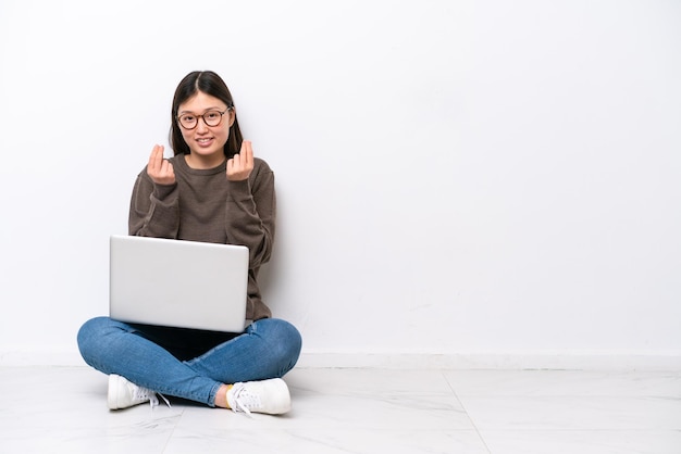 Jonge vrouw met een laptop die op de vloer zit en geldgebaar maakt