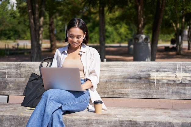 Foto jonge vrouw met een laptop terwijl ze op een bankje zit