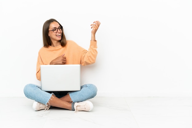 Jonge vrouw met een laptop zittend op de vloer gitaar gebaar maken