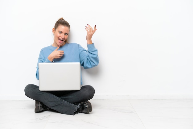 Jonge vrouw met een laptop zittend op de vloer gitaar gebaar maken