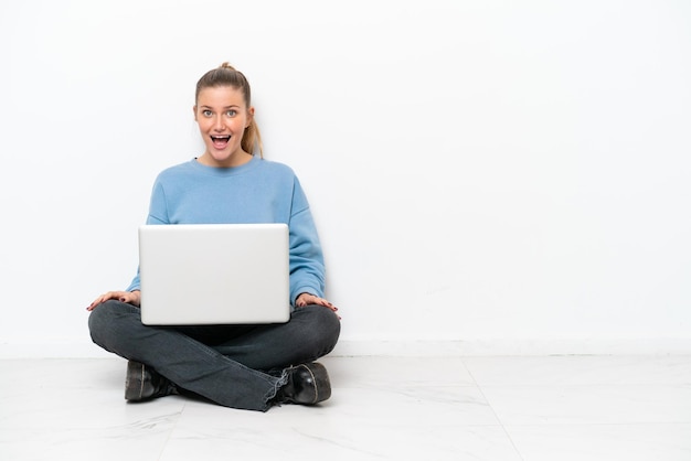 Jonge vrouw met een laptop zittend op de vloer met verrassing gezichtsuitdrukking