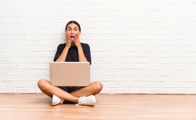 Jonge vrouw met een laptop zittend op de vloer met verrassing gezichtsuitdrukking