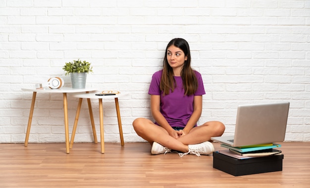 Jonge vrouw met een laptop zittend op de vloer op binnenshuis met twijfels tijdens het kijken kant