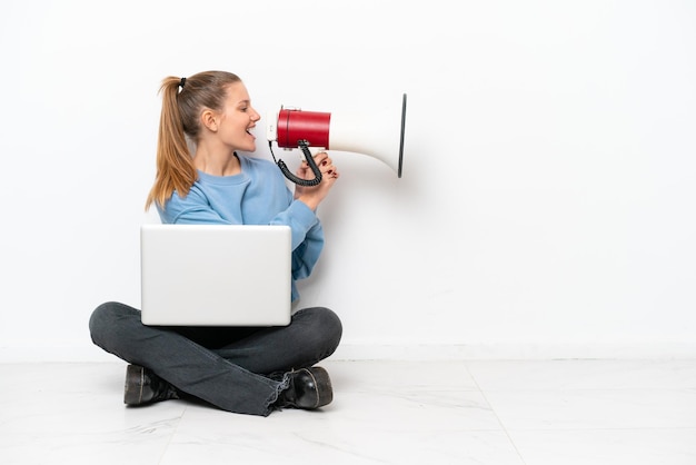 Jonge vrouw met een laptop zittend op de vloer schreeuwen door een megafoon