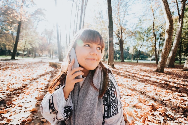 Jonge vrouw met een leuk gesprek tijdens een zonsondergang in het bos tijdens een herfstachtige winterdag. Connectiviteit en sociaal concept. Jongeren levensstijl. Vrienden online begroeten. Ruimte kopiëren.