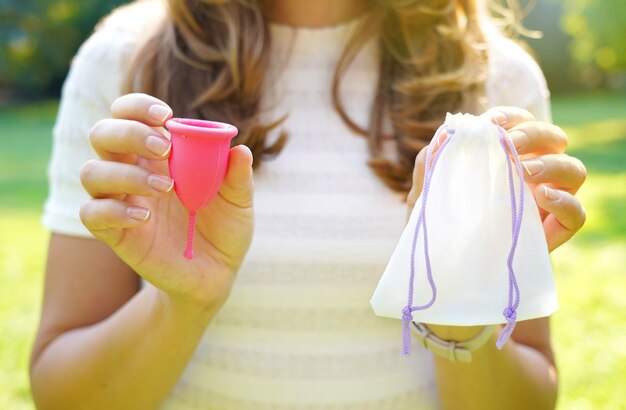 Jonge vrouw met een menstruatiecup met tas die tegen een groene natuurlijke achtergrond staat