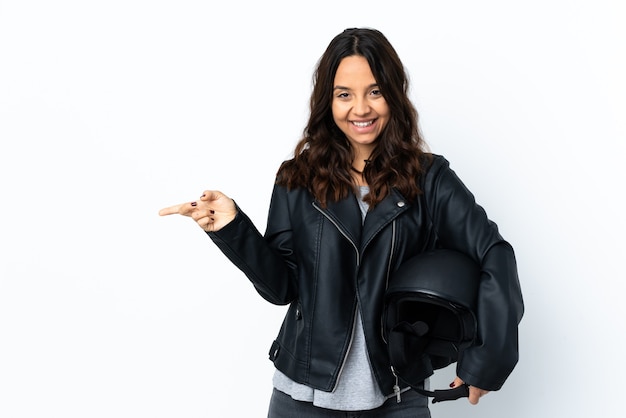 Jonge vrouw met een motorhelm over geïsoleerde witte muur wijzende vinger naar de zijtakken en gelukkig