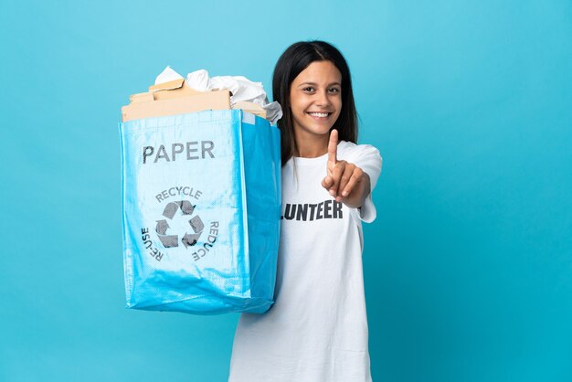 Jonge vrouw met een recycling zak vol papier laten zien en een vinger opheffen