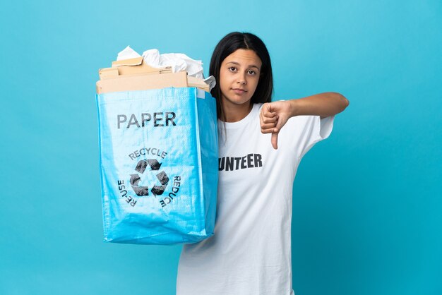 Jonge vrouw met een recycling zak vol papier met duim omlaag met negatieve uitdrukking