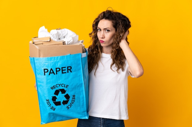 Jonge vrouw met een recycling zak vol papier om te recyclen geïsoleerd op gele muur twijfels
