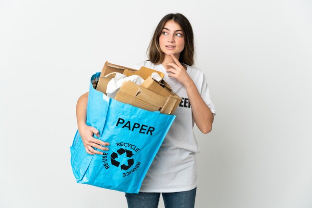 Jonge vrouw met een recycling zak vol papier om te recyclen geïsoleerd op wit opzoeken tijdens het glimlachen