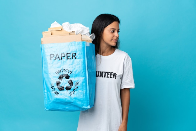 Jonge vrouw met een recycling zak vol papier op zoek naar de zijkant