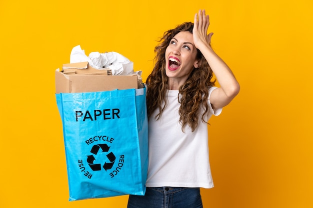 Jonge vrouw met een recyclingzak vol papier om te recyclen geïsoleerd op geel heeft iets gerealiseerd en de oplossing voor ogen