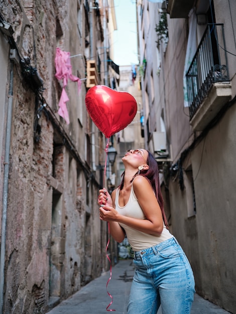 Jonge vrouw met een rode hartvormige ballon buiten op straat. Valentijnsdag concept.