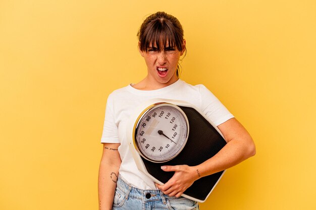 Jonge vrouw met een schaal geïsoleerd op gele achtergrond schreeuwen erg boos en agressief.