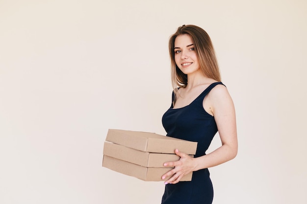 Jonge vrouw met een stapel dozen in haar handen Pizzabezorger op een beige achtergrond