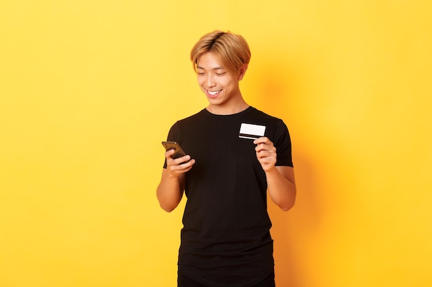 Jonge vrouw met een telefoon terwijl ze tegen een gele achtergrond staat