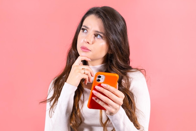 Jonge vrouw met een vermaakte en glimlachende uitdrukking geniet van het scrollen van sociale media op een oranje smartphone lo