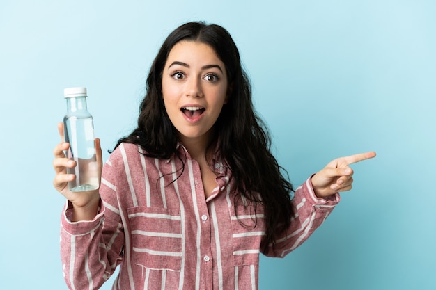 Jonge vrouw met een water geïsoleerd op blauwe achtergrond verrast en wijzende vinger naar de zijkant