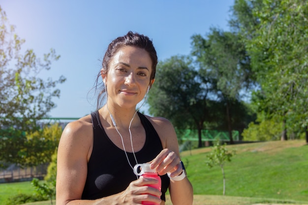 Jonge vrouw met een waterfles in haar hand lacht naar de camera en rust uit na het hardlopen