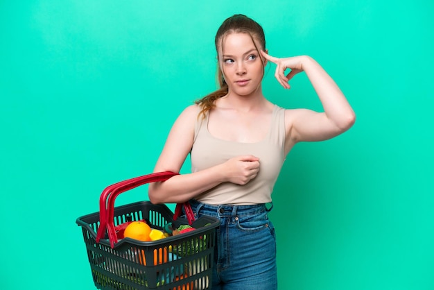 Jonge vrouw met een winkelmandje vol voedsel geïsoleerd op groene achtergrond