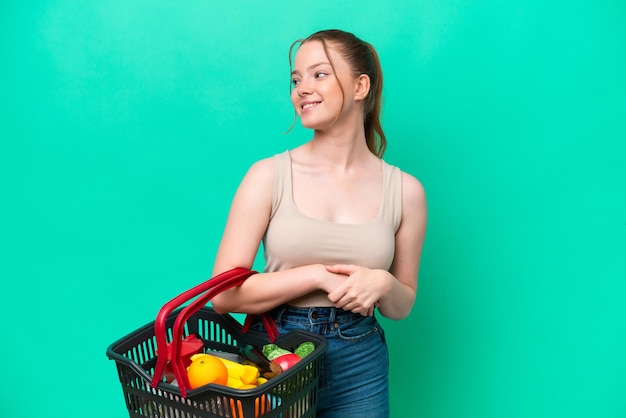 Jonge vrouw met een winkelmandje vol voedsel geïsoleerd op groene achtergrond