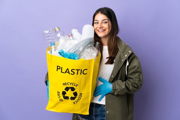 Jonge vrouw met een zak vol plastic flessen om paars te recyclen, lachend veel