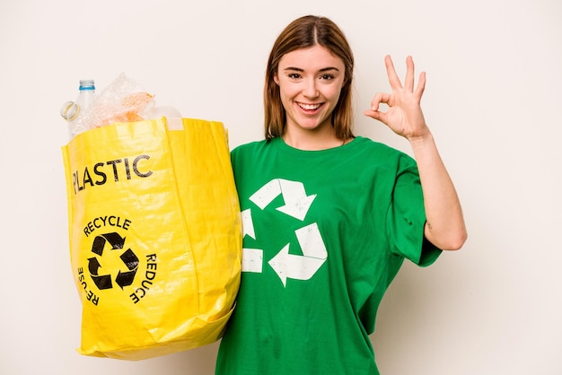 Jonge vrouw met een zak vol plastic flessen om te recyclen geïsoleerd op een witte achtergrond, vrolijk en zelfverzekerd met een goed gebaar