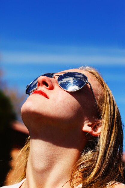 Jonge vrouw met een zonnebril die naar de hemel kijkt