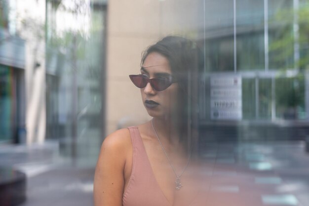 Foto jonge vrouw met een zonnebril gezien door een glazen raam in de stad