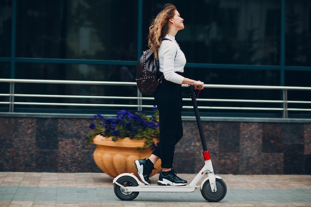 Jonge vrouw met elektrische autoped bij de stad