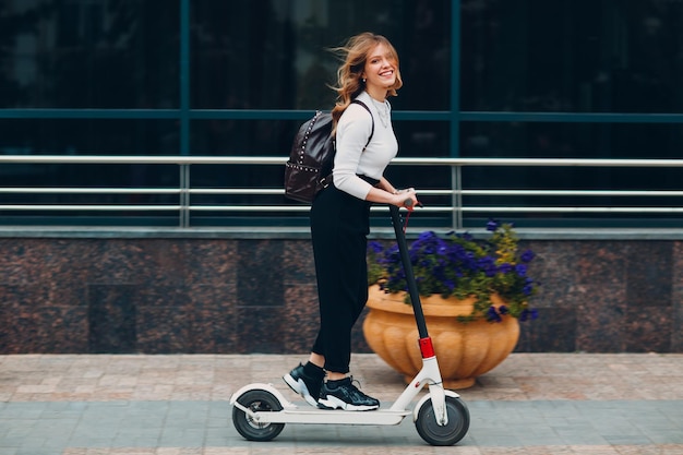 Jonge vrouw met elektrische autoped bij de stad