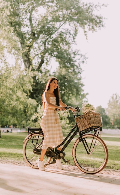 Jonge vrouw met elektrische fiets en bloemen in de mand