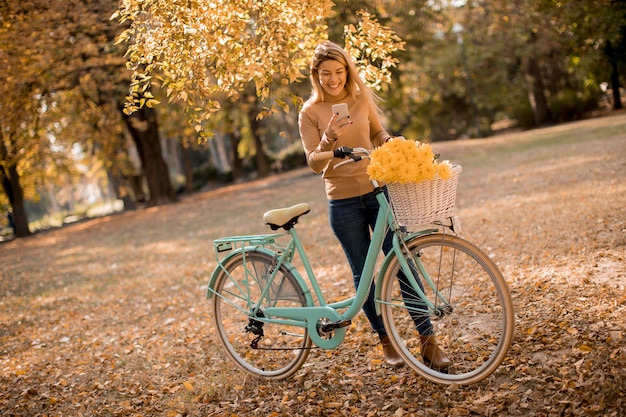 Jonge vrouw met fiets die smartphone in de herfstpark gebruiken