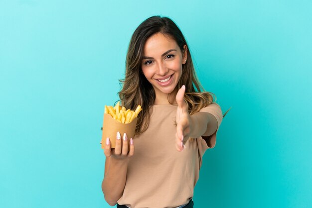 Jonge vrouw met gebakken chips over geïsoleerde achtergrond handen schudden voor het sluiten van een goede deal